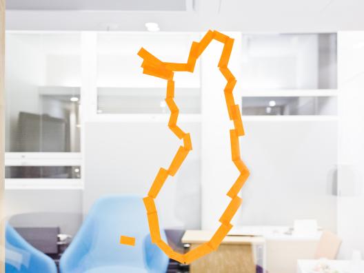Suomen kartan ääriviivat piirrettynä lasiin. Takana näkyy odotushuone. 