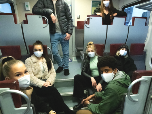 Nuorisoa junalla maskit kasvoilla. 