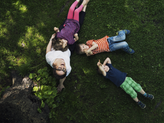Hyvän mielen kunta -kuvituskuva. Neljä ihmistä makaa nurmikolla, kuvattu ylhäältäpäin. 