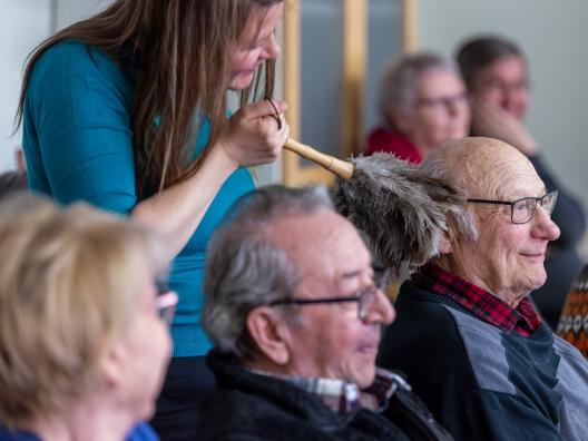 Kuvassa nainen kutittelee seniorin hiuksia huiskulla. 