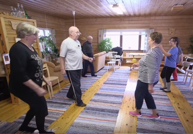Ikäihmiset jumppaavat ryhmänä kodin olohuoneessa