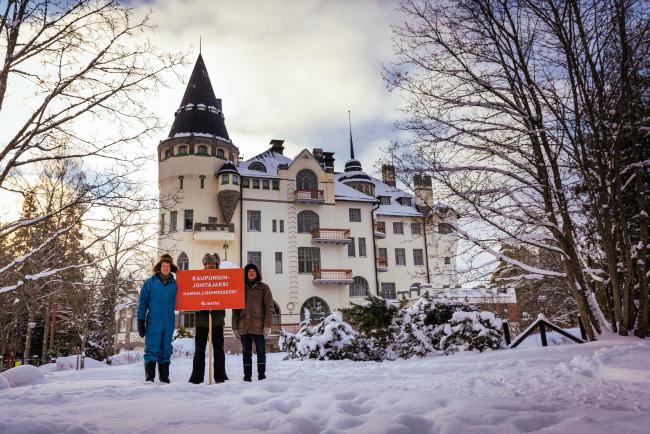 Imatran bändi Valtiohotellin edessä Kaupungin johtajaksi kansallisihmeeseen -kyltin kanssa.