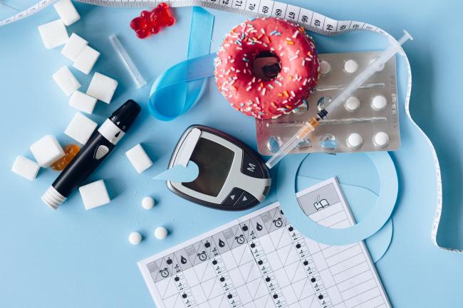 Kuvassa diabeteksen hoitoon liittyviä välineitä, lääkkeitä, kalenteri, sokeria ja donitsi
