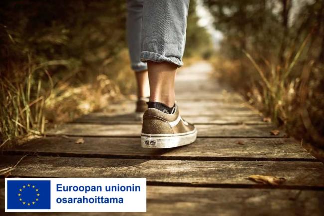 Ihminen kävelee puisella polulla, vain jalat näkyvät, alareunassa sininen EU-lippulogo ja teksti jossa lukee: Euroopan unionin osarahoittama