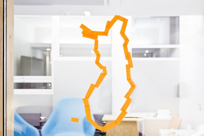 Suomen kartan ääriviivat piirrettynä lasiin. Takana näkyy odotushuone. 