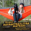 Mainos, jossa nainen istuu riippumatossa kahden koiran kanssa.