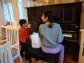 Kolme eri ikäistä lasta soittaa yhdessä pianoa.