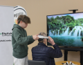 Opiskelija opastaa VR-laseilla tapahtuvalle nojatuolimatkalle istahtanutta kävijää.